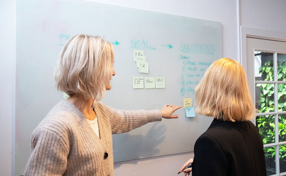 UX designers pointing to post-it note on whiteboard planning website experience